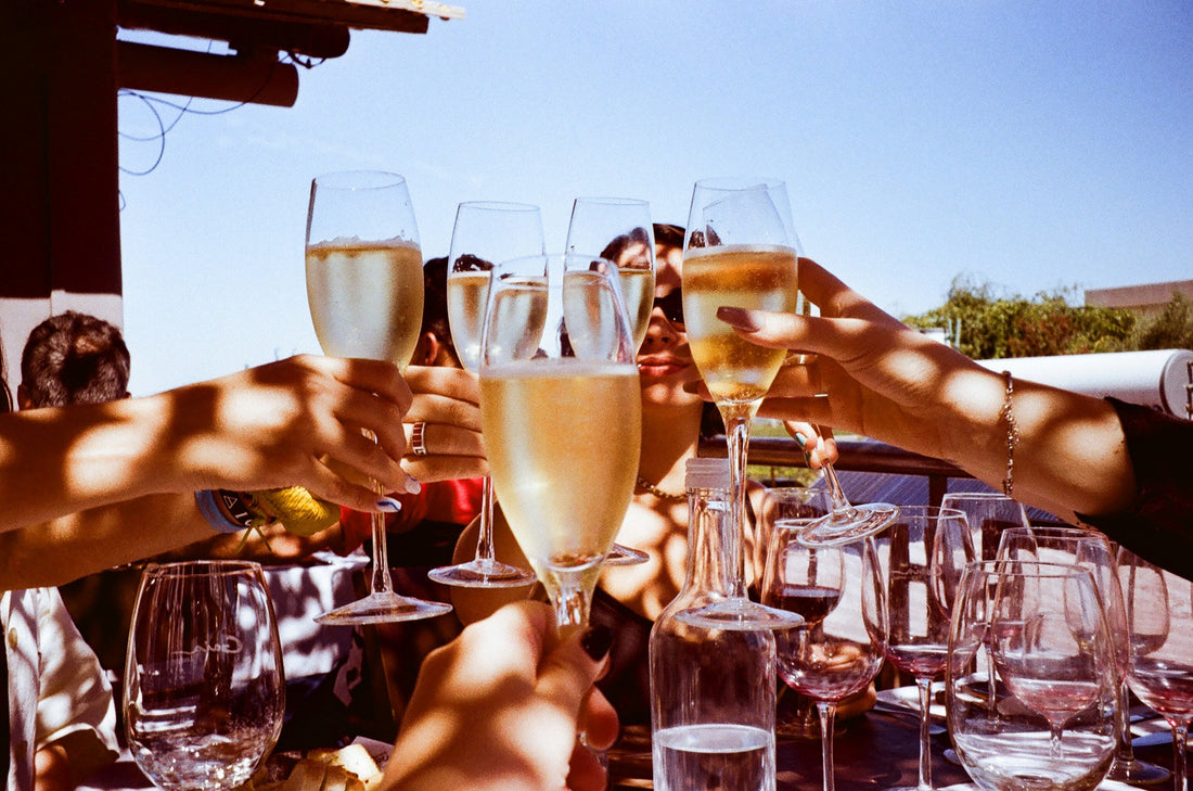 4 people toasing with champagne glasses sitting around a table with more champagne glasses and food on the table